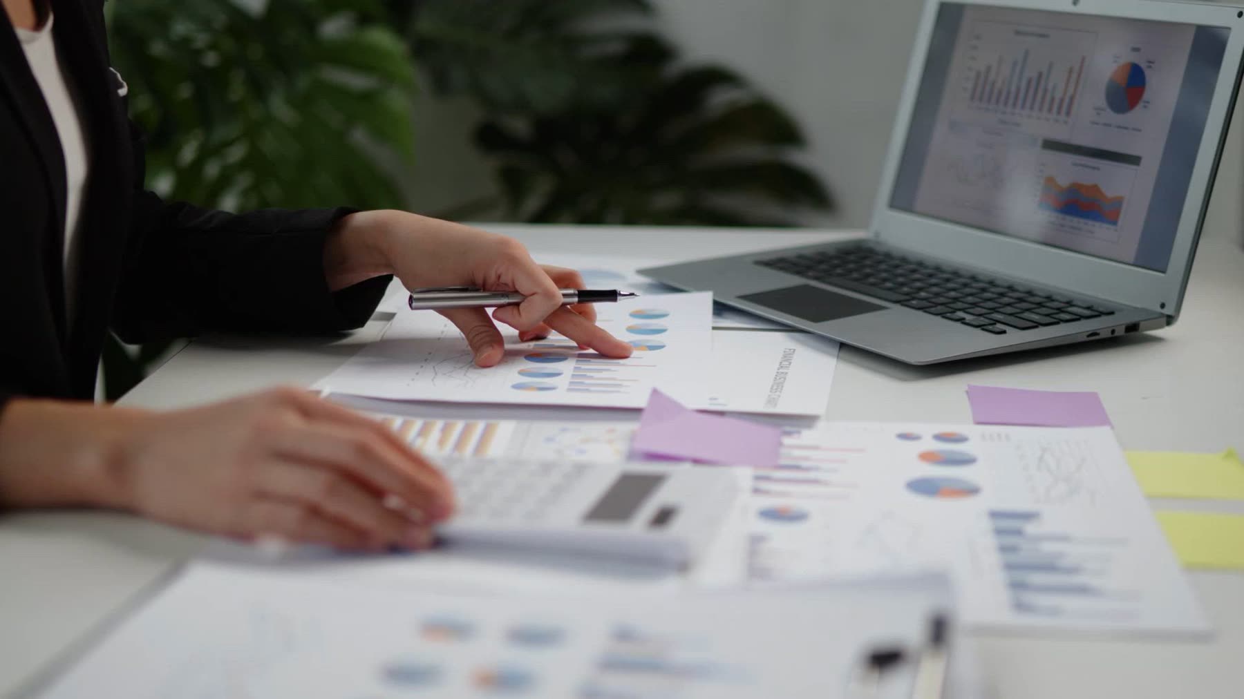 An accountant marks up printed financial charts beside a laptop showing the same reports.
