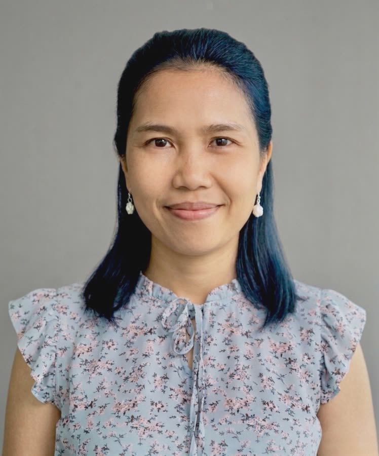 Rowena Constantino, in a floral blouse, smiling against a grey background.