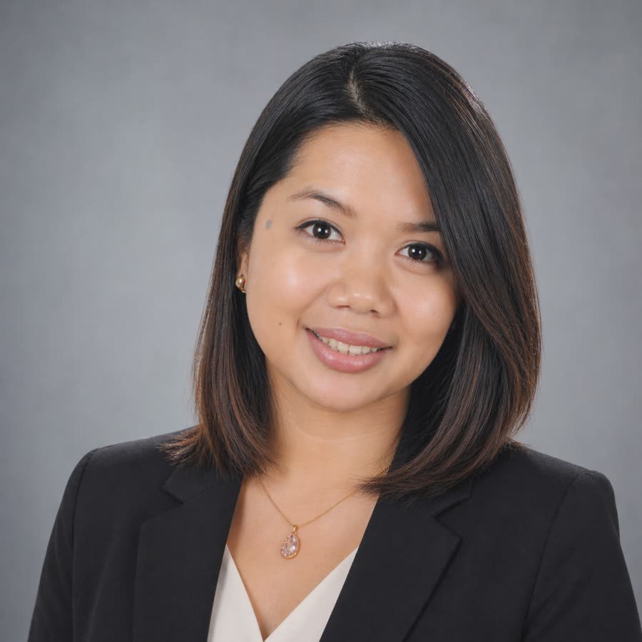 Shelah Ohoylan, in a black blazer, smiling against a grey studio background.