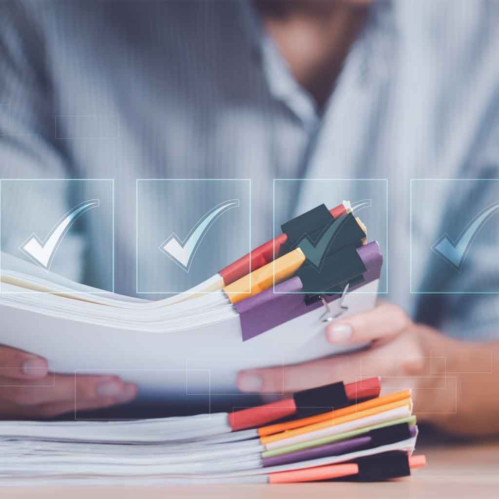 A person holds a stack of documents tabbed with coloured markers.